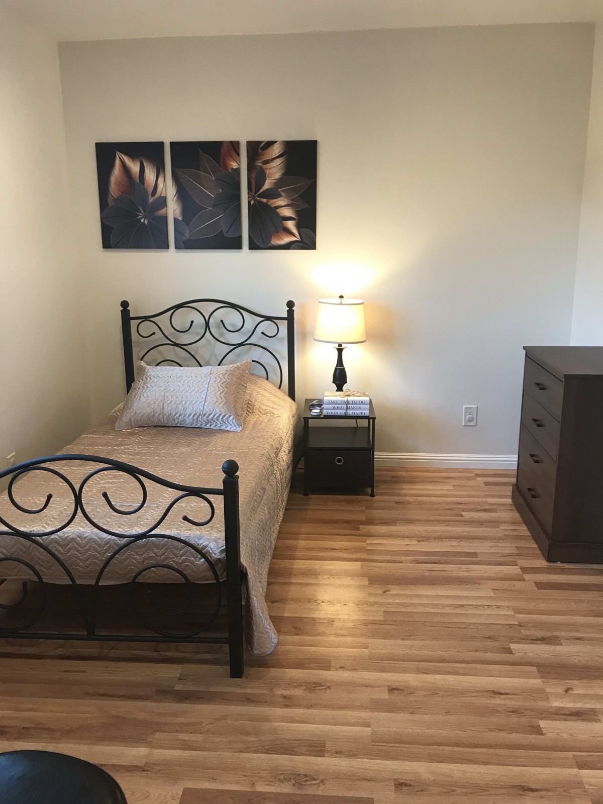 A minimalist bedroom with a single bed, bedside lamp, and a dresser.