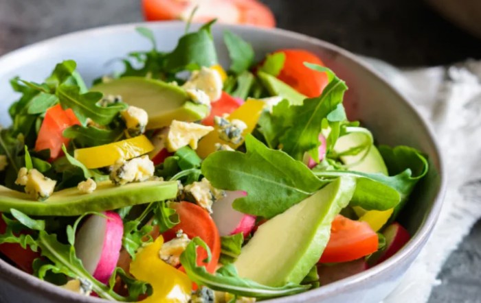 A vibrant and fresh salad with avocado, arugula, bell peppers, and tomatoes.