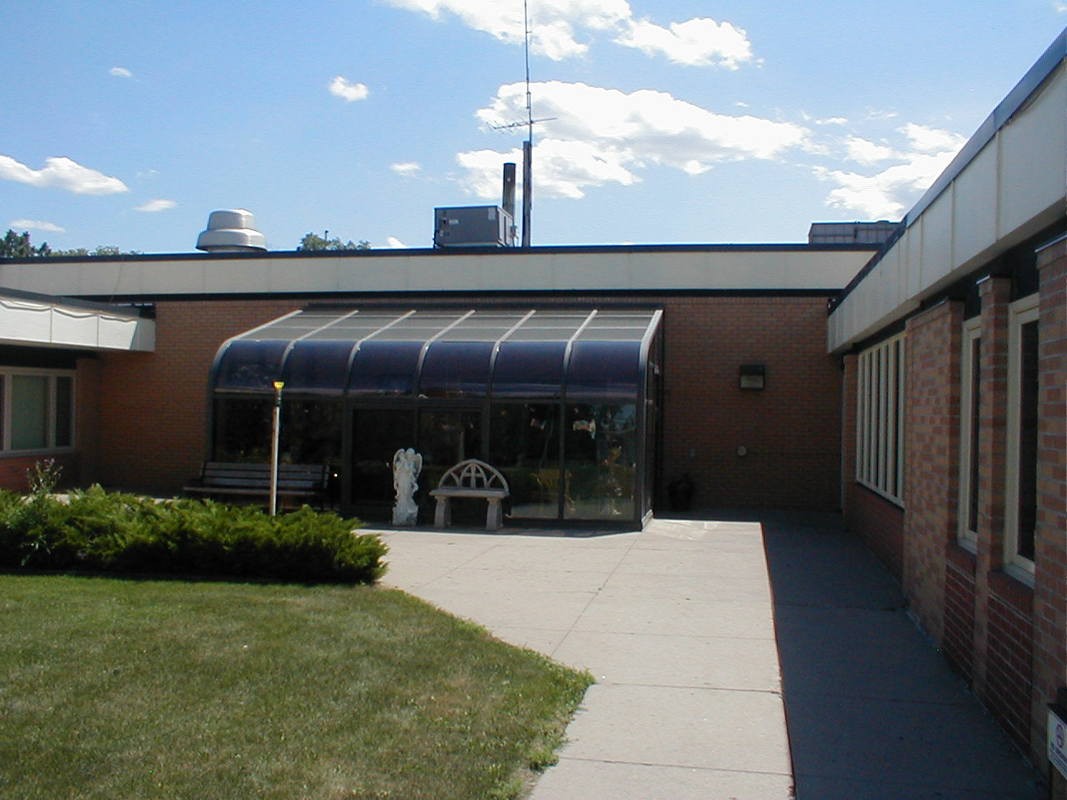 A brick building featuring a small greenhouse extension with a bench outside under a clear blue sky.