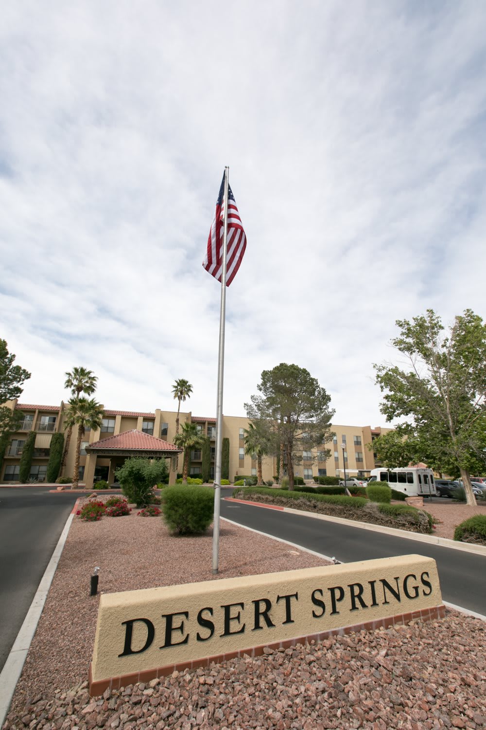 A building with a flagpole displaying the American flag set against a cloudy sky and surrounded by desert landscaping.
