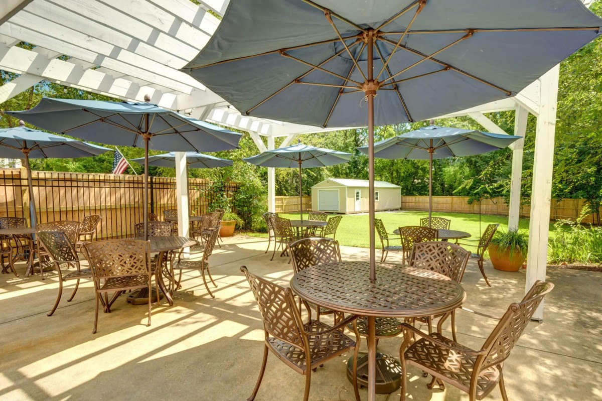 A sunny outdoor patio with tables, chairs, and umbrellas overlooking a garden.