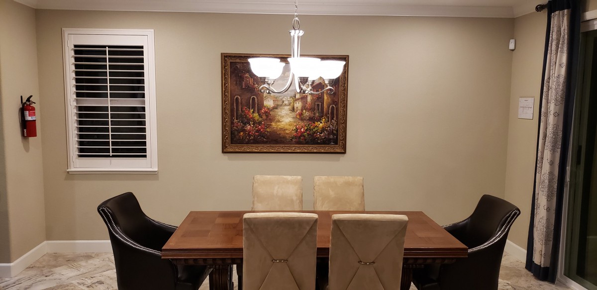 A dining room with a wooden table, four beige chairs, and a painting on the wall.