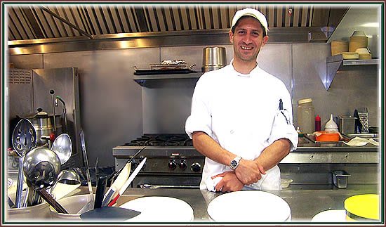 A chef smiling in a restaurant kitchen.