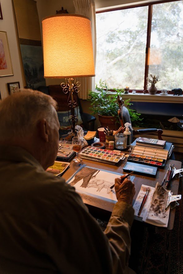 An artist working on a painting in a cozy studio filled with art supplies, books, and plants by the window.