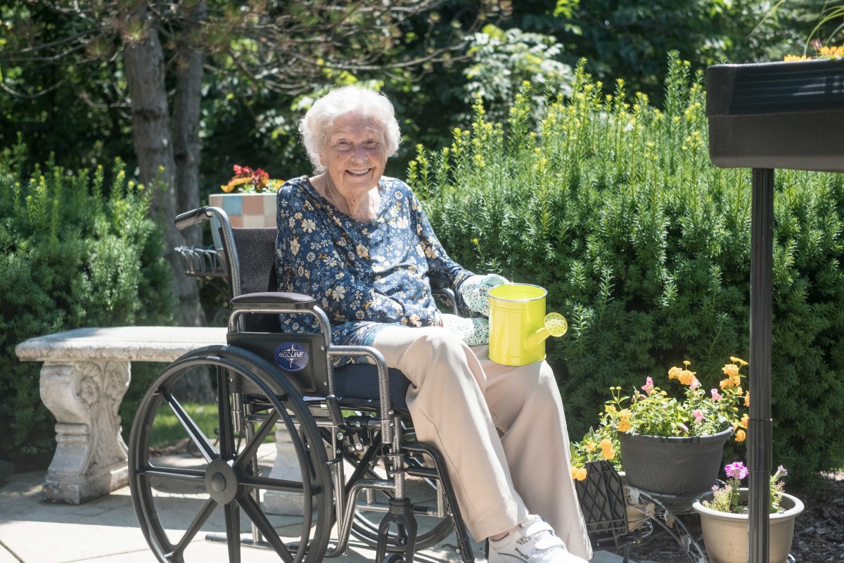 An elderly person sitting in a wheelchair, enjoying a sunny day in the garden.