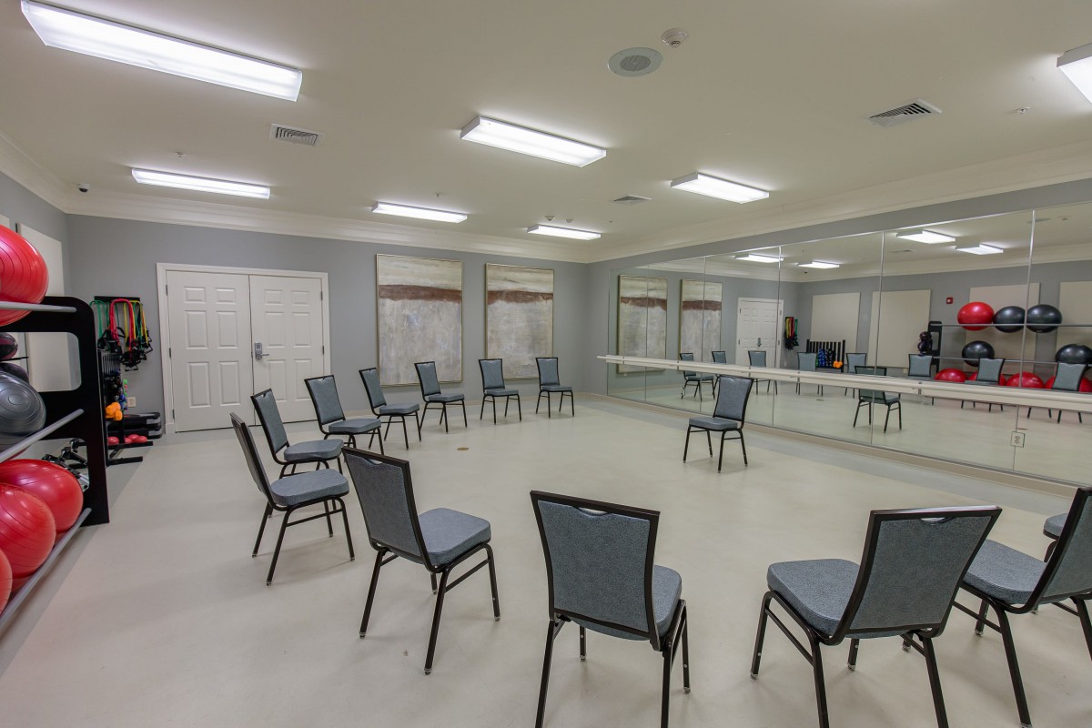 An empty room with chairs arranged in a circle, featuring mirrors on one wall.