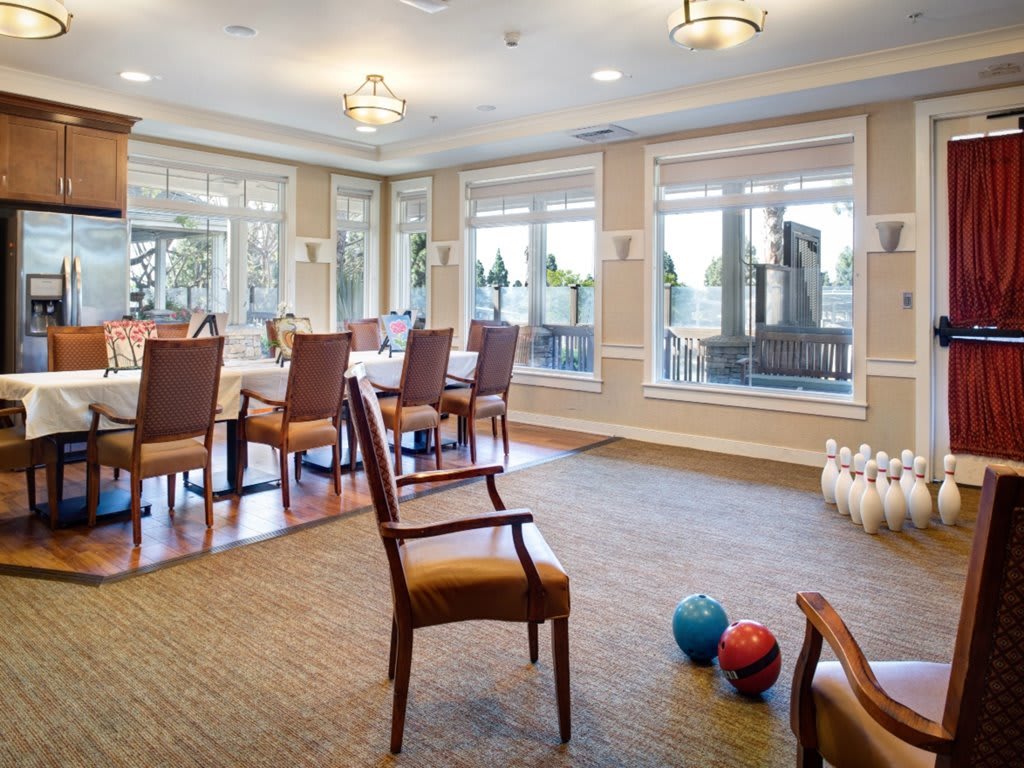 A spacious dining and activity room featuring set tables, chairs, and a corner with bowling pins and balls.