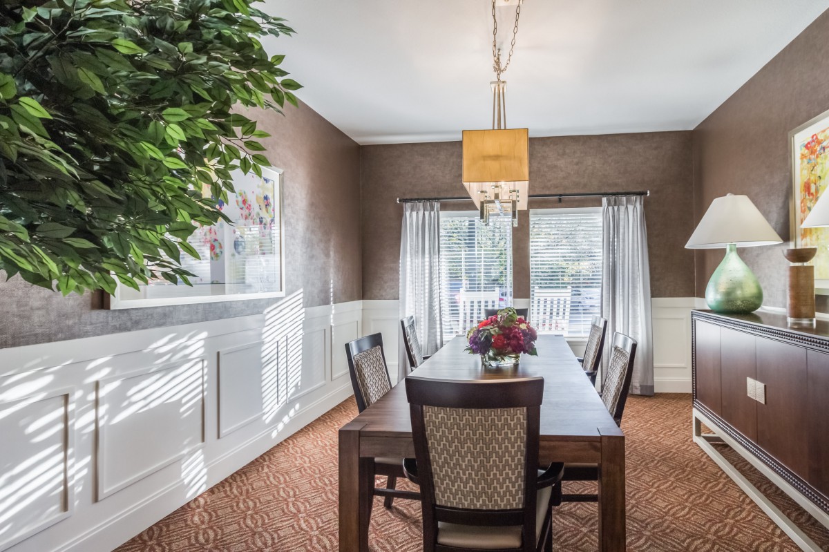 A well-lit dining room featuring a wooden table, chairs, and a chandelier.
