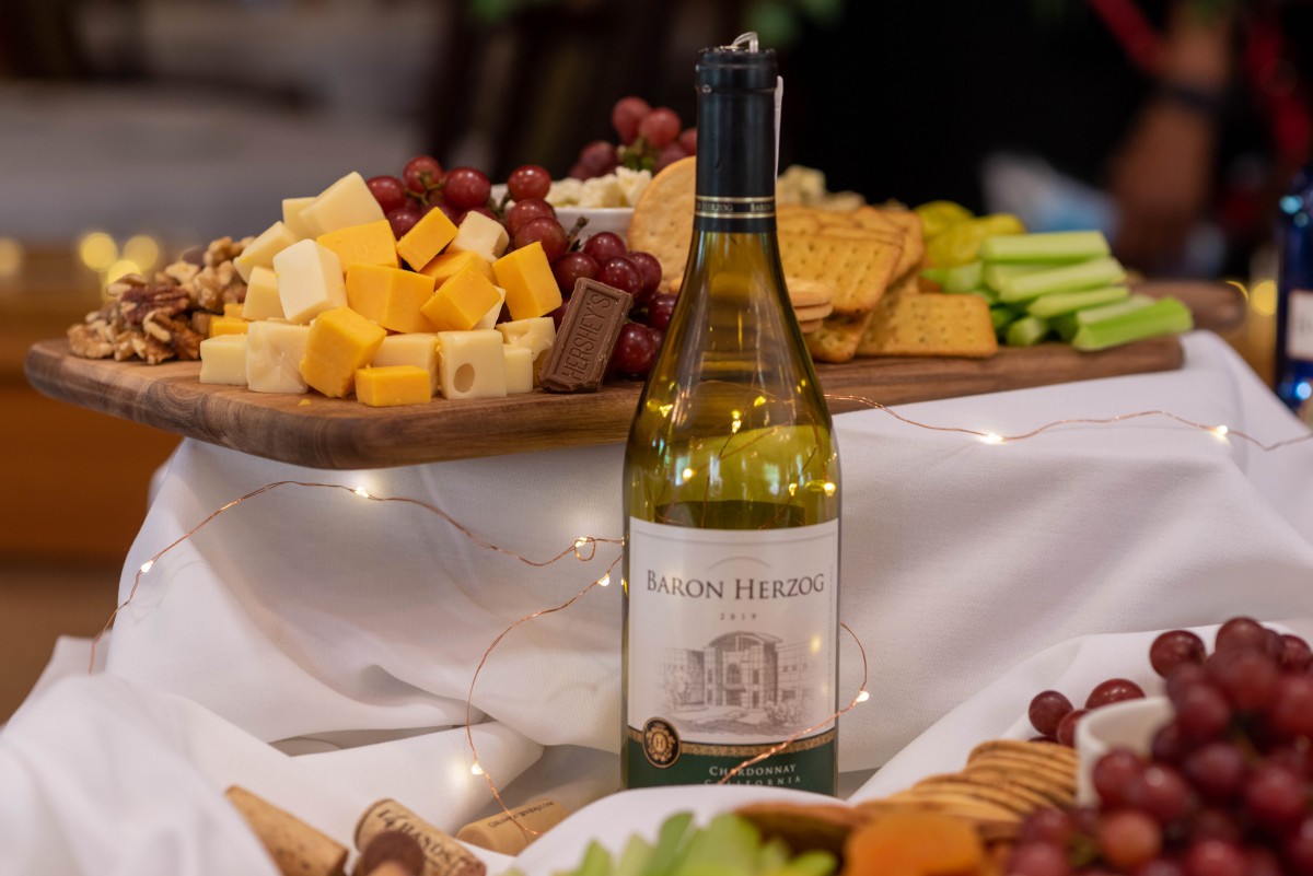 A bottle of wine displayed on a table surrounded by a variety of cheeses, grapes, and crackers.