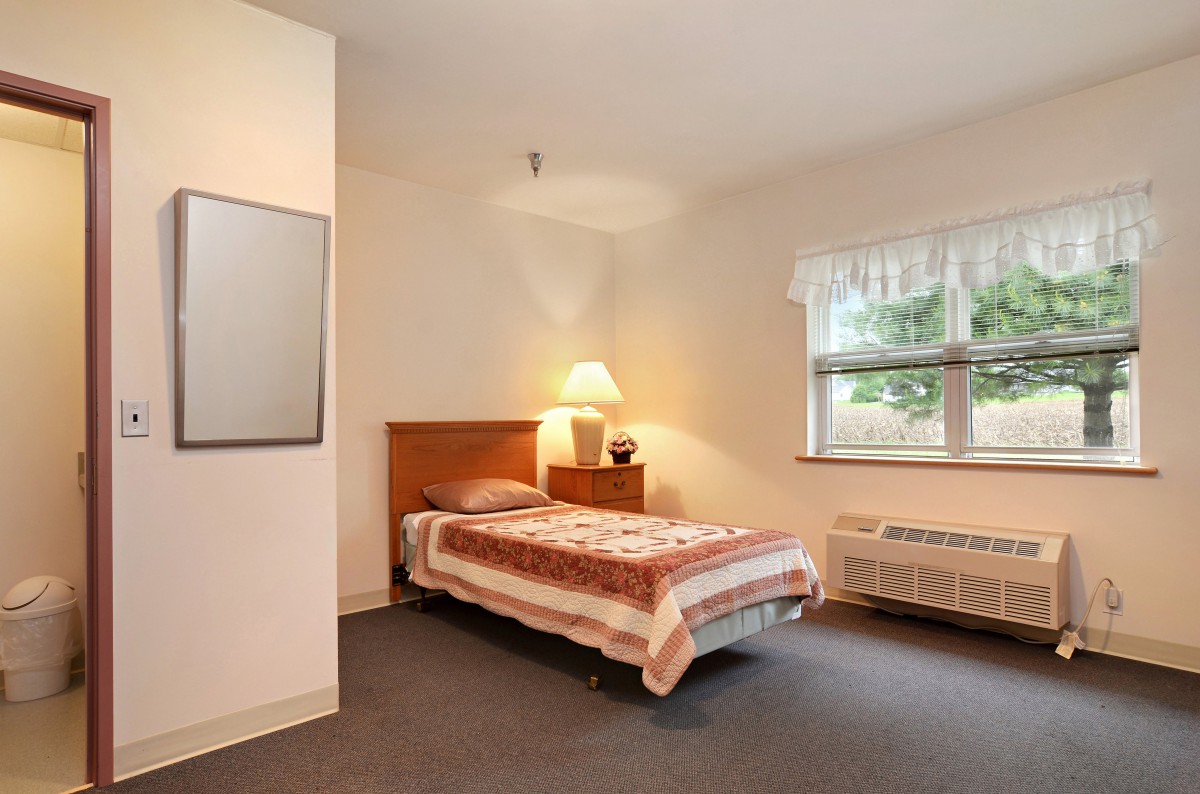 A minimalist bedroom with a single bed, lamp, and window.