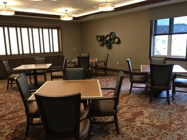 A cozy dining area with multiple tables and chairs, featuring a patterned carpet and warm lighting.