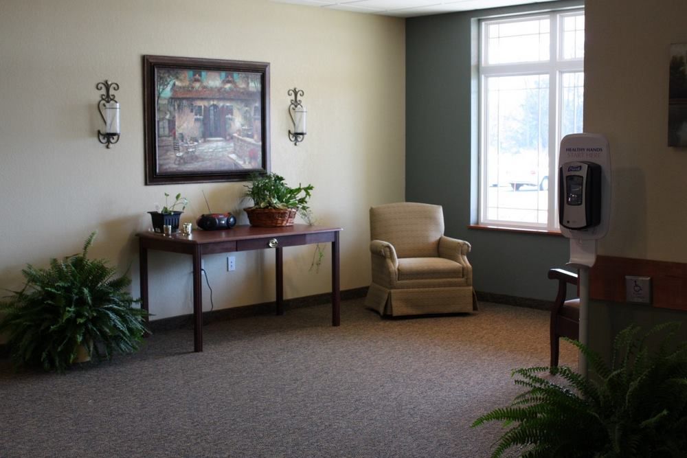 A cozy living room with a comfortable chair and table, decorated with plants and artwork.