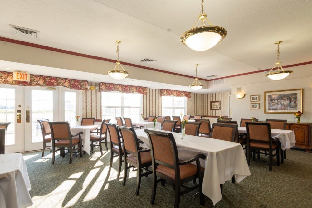 A well-lit dining room with arranged tables and chairs, decorated with elegant lighting and large windows.