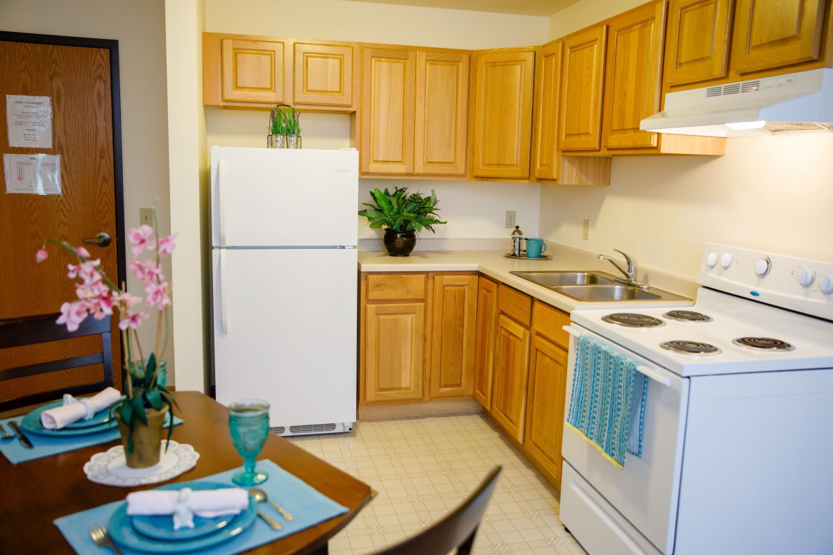 A cozy kitchen with wooden cabinets, white appliances, and a small dining setup.