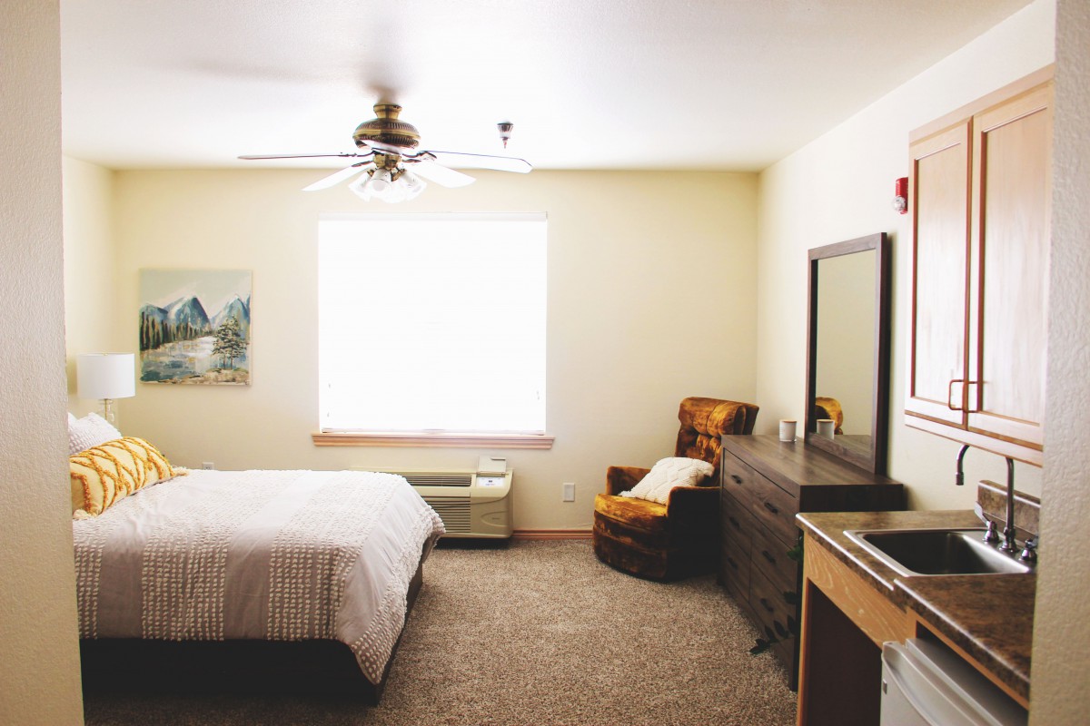 A cozy bedroom with a bed, chair, dresser, and ceiling fan.