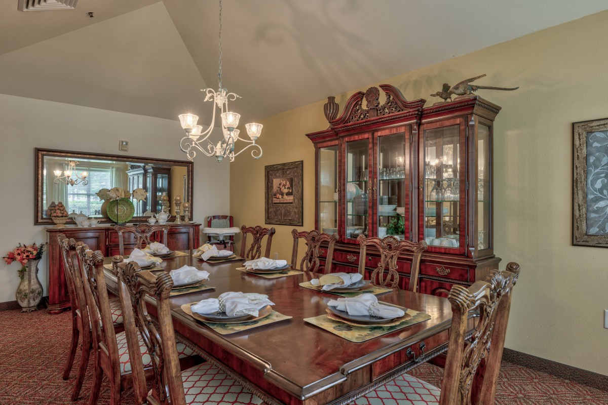 A traditional dining room with a wooden table set for a meal, surrounded by elegant chairs and illuminated by a chandelier.
