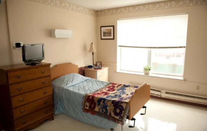 A cozy bedroom with a single bed, a colorful quilt, and natural light coming through the window.