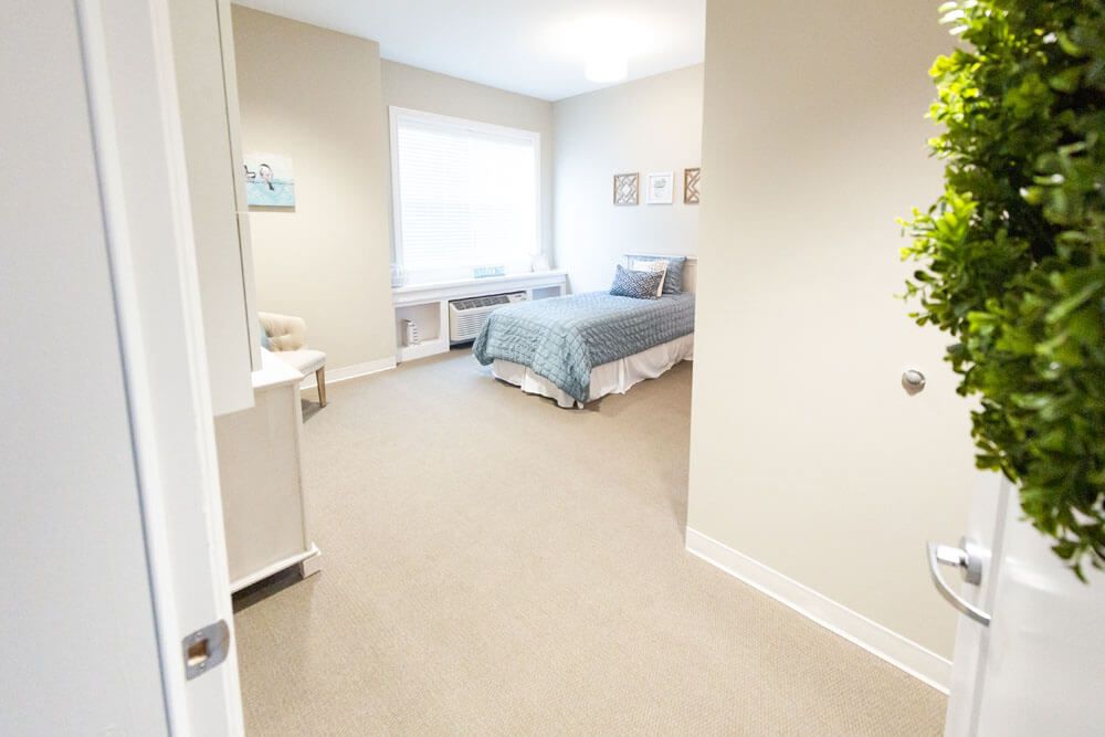 A bright and minimalist bedroom with a neatly made bed and a large window letting in natural light.