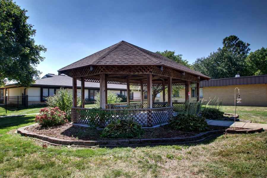 A scenic view of a wooden gazebo surrounded by greenery in a garden setting.