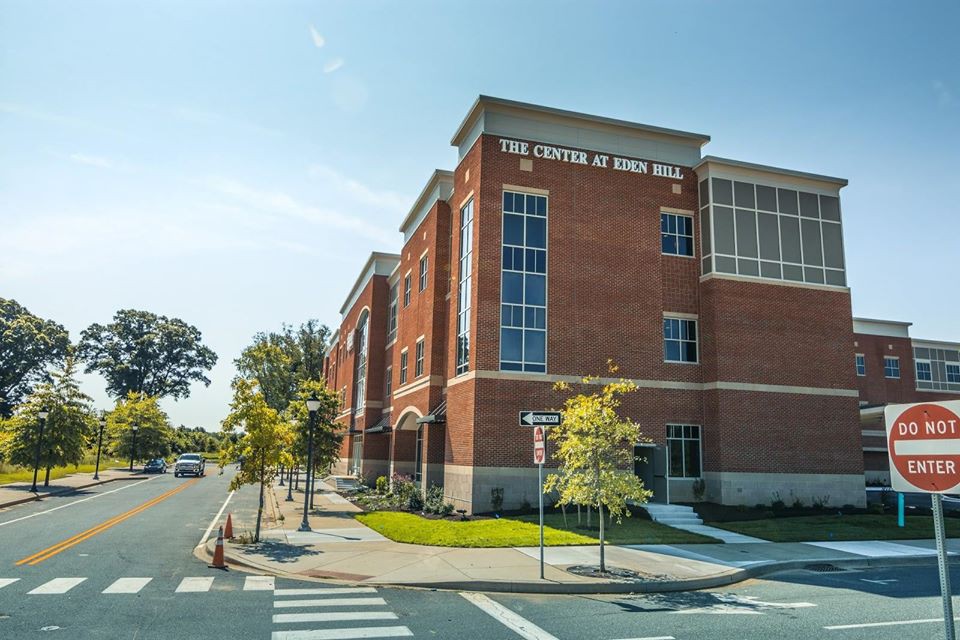 A red brick building with a clear blue sky in the background, surrounded by trees and a crosswalk in front.