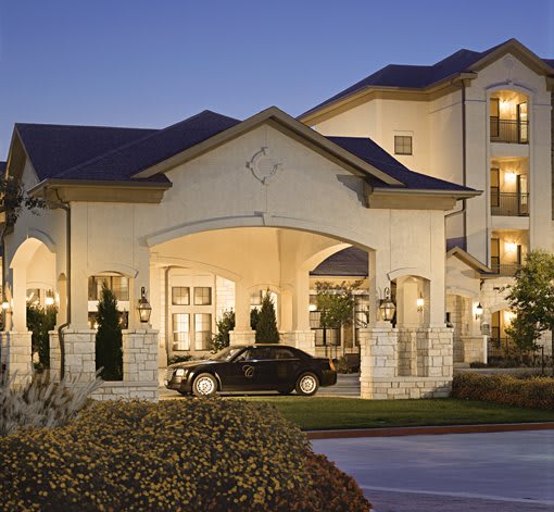 An elegant hotel entrance with a car parked under the porte-cochre during the evening.
