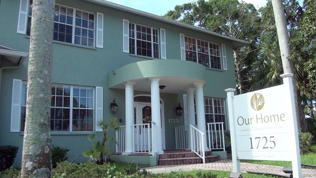 A green two-story building with a columned entrance and large windows.