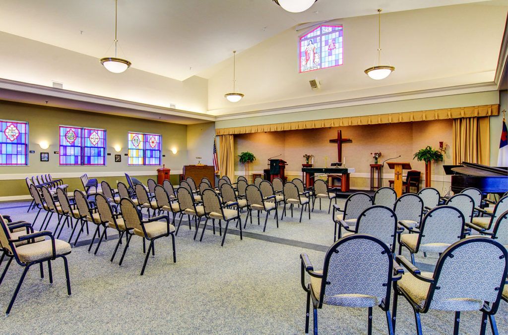 An interior view of a church chapel with rows of chairs and stained glass windows.