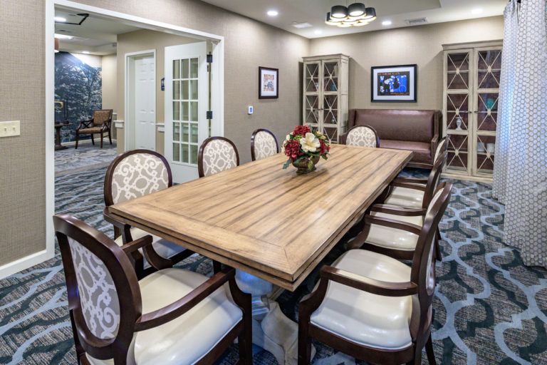 A modern dining room with a large wooden table surrounded by elegant chairs, featuring a flower arrangement as the centerpiece.