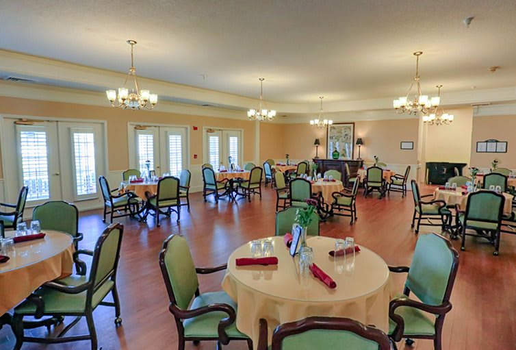 A spacious and elegantly furnished dining room with multiple round tables set with tablecloths.