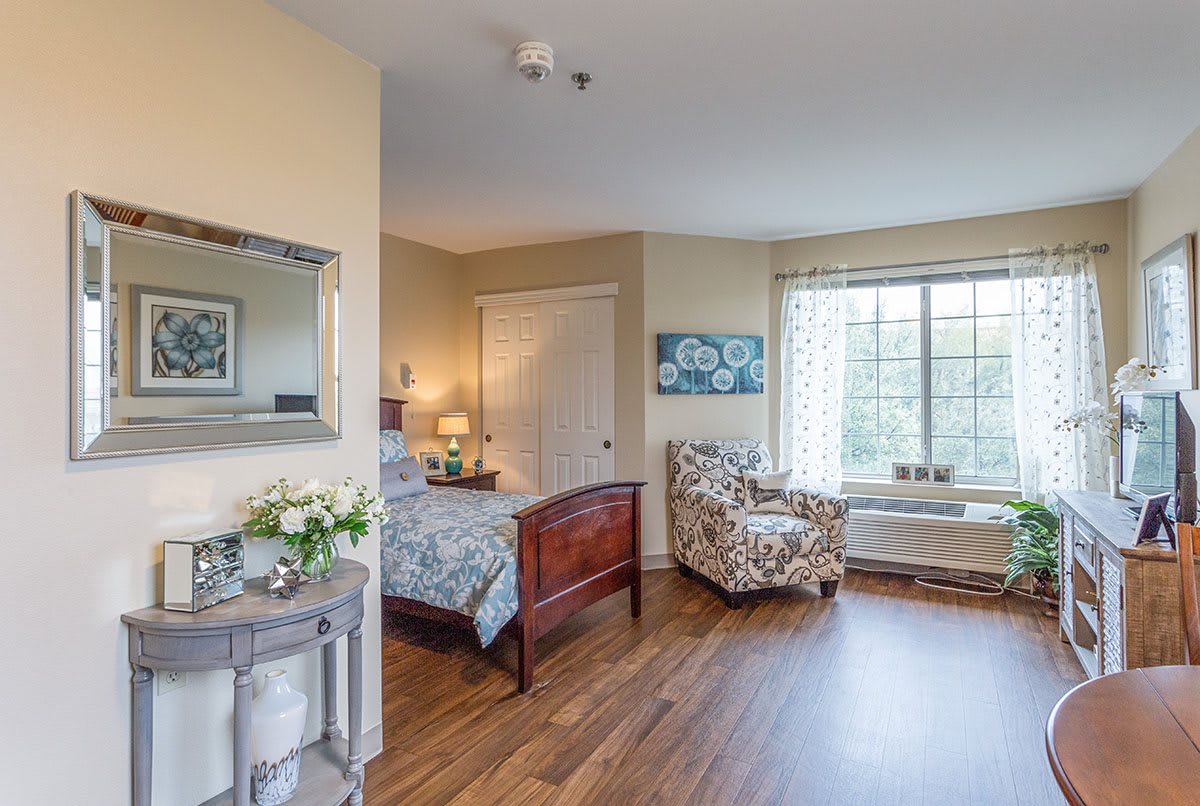 A cozy bedroom with a wooden bed, armchair, and large window.