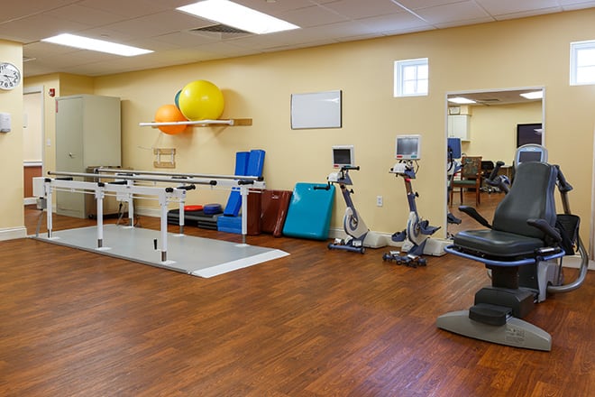 A physical therapy room equipped with various exercise equipment, including therapy balls and stationary bikes.
