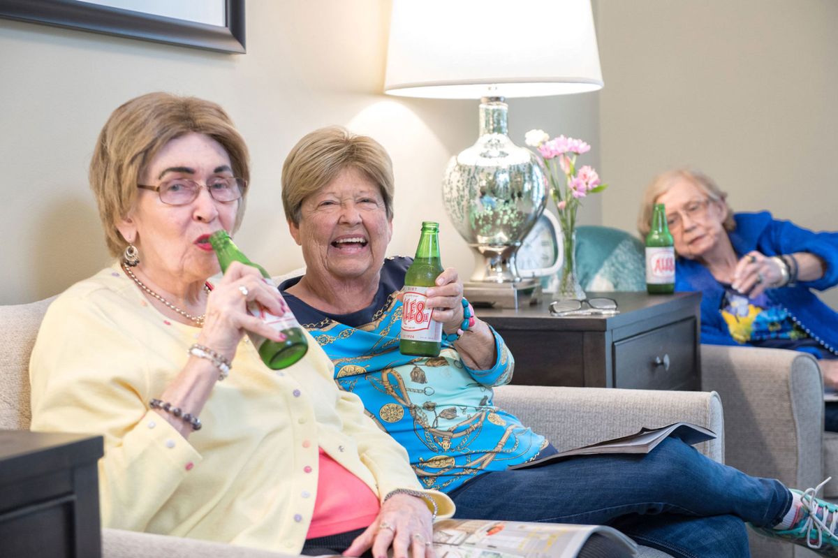 A group of senior friends enjoying drinks and sharing a laugh together indoors.