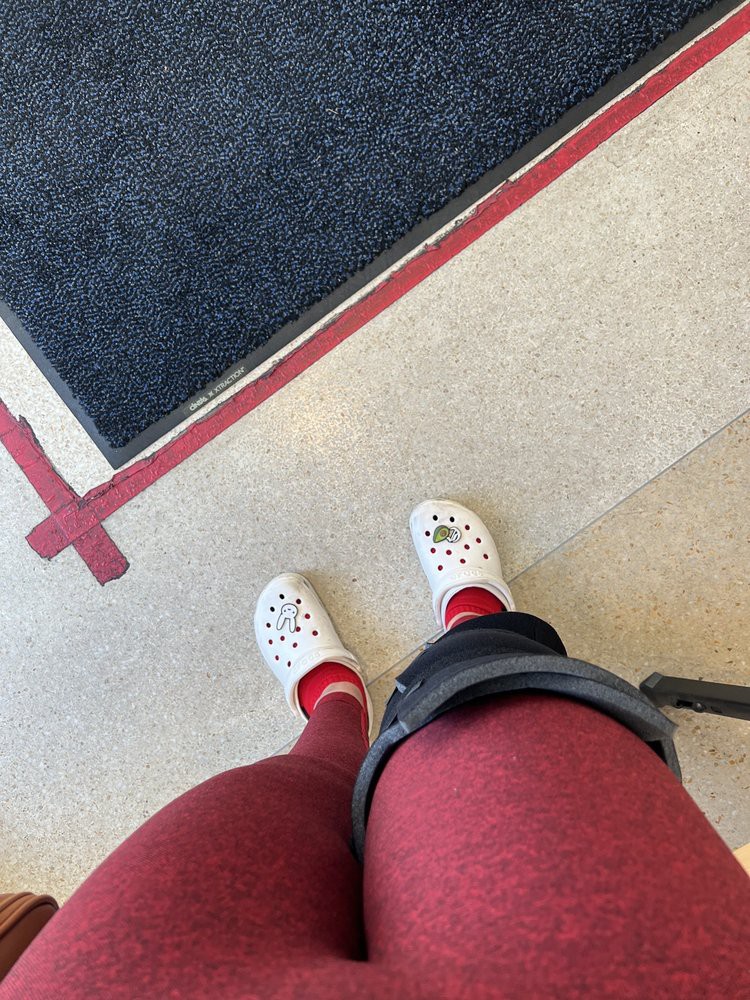 A person wearing red leggings and white shoes with a leg brace is standing indoors.
