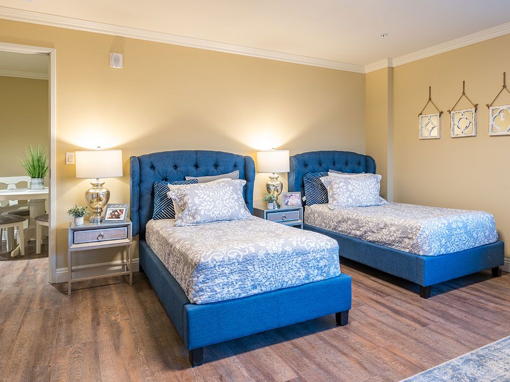 A modern bedroom featuring twin beds with blue headboards and elegant decor.