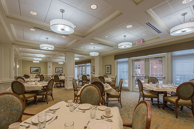 An elegant dining room with tables and chairs arranged neatly, featuring sophisticated lighting.