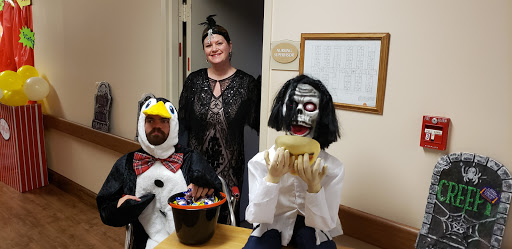 A festive Halloween gathering featuring a woman in costume alongside two puppets, one dressed as a penguin and the other in a spooky outfit.