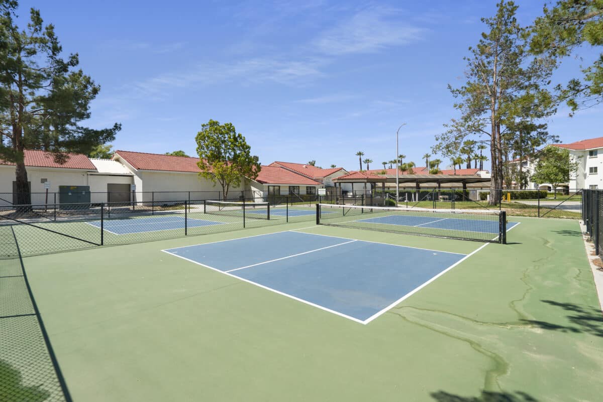 Outdoor tennis courts surrounded by trees and nearby buildings on a sunny day.