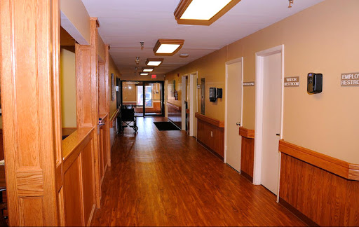 A well-lit hospital hallway with wooden flooring, showcasing doors and a waiting area.