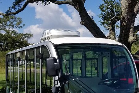 A parked bus under a tree on a clear day.