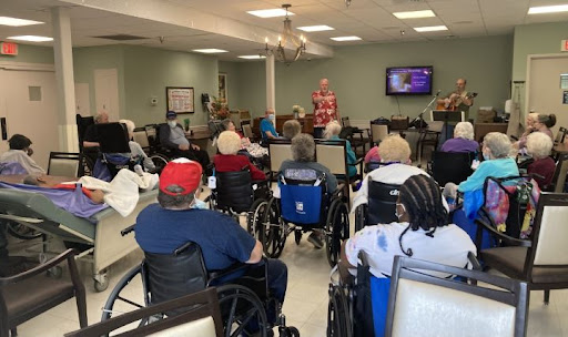 A lively community event taking place in a senior living facility, where a speaker engages with the audience of residents.