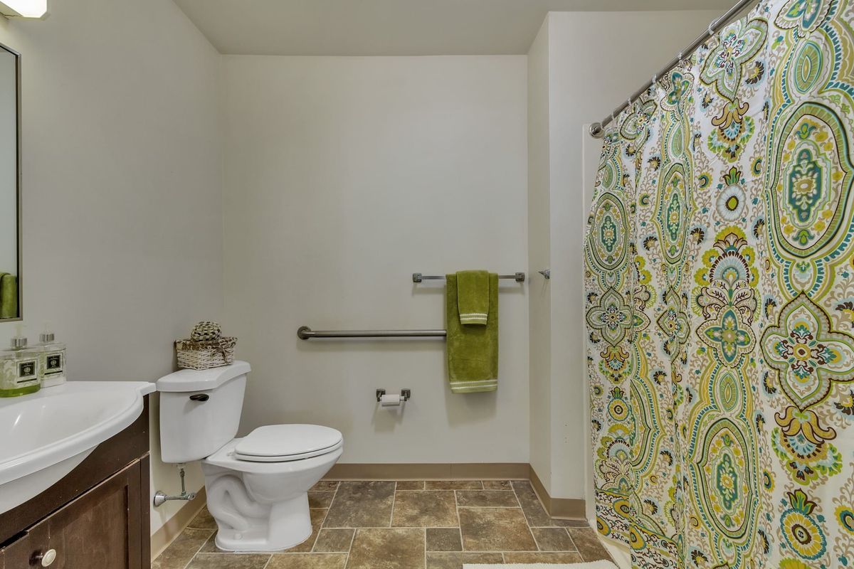 A bathroom with a toilet, patterned shower curtain, and green towel hanging on a grab bar.
