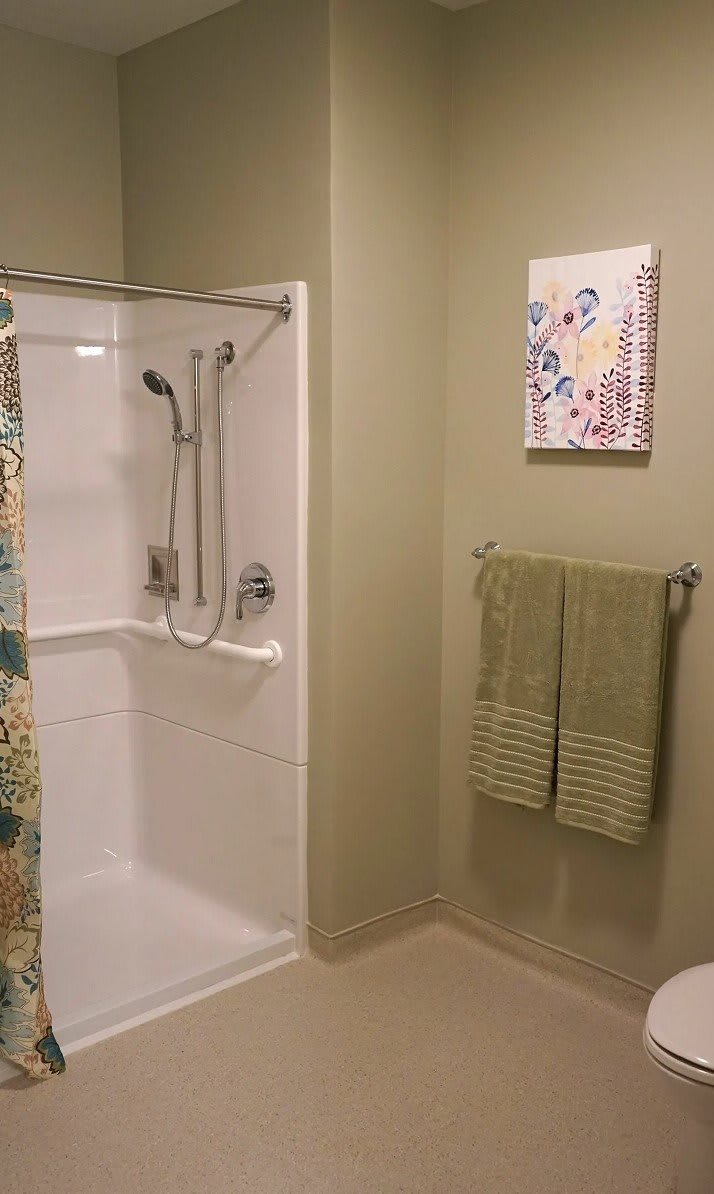 A bathroom featuring a modern shower setup, green towels, and colorful wall art.