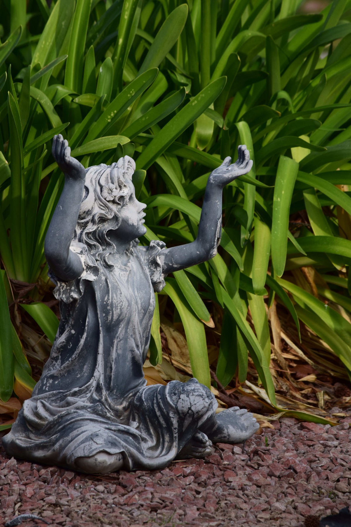 A garden statue of a figure with raised arms surrounded by lush greenery.