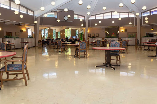 A spacious common area featuring tables and chairs, illuminated by natural light from large windows.