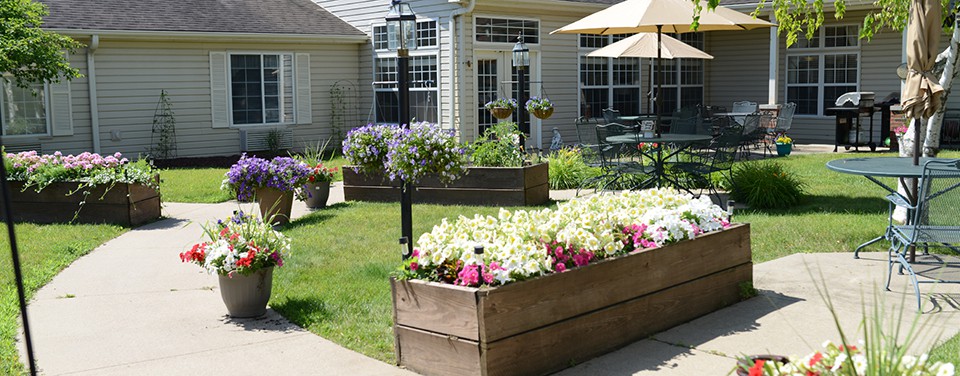 A sunny patio area with raised flower beds filled with colorful blooms, surrounded by a well-maintained garden.