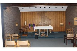 A simple church interior with an altar, wooden paneling, and seating.