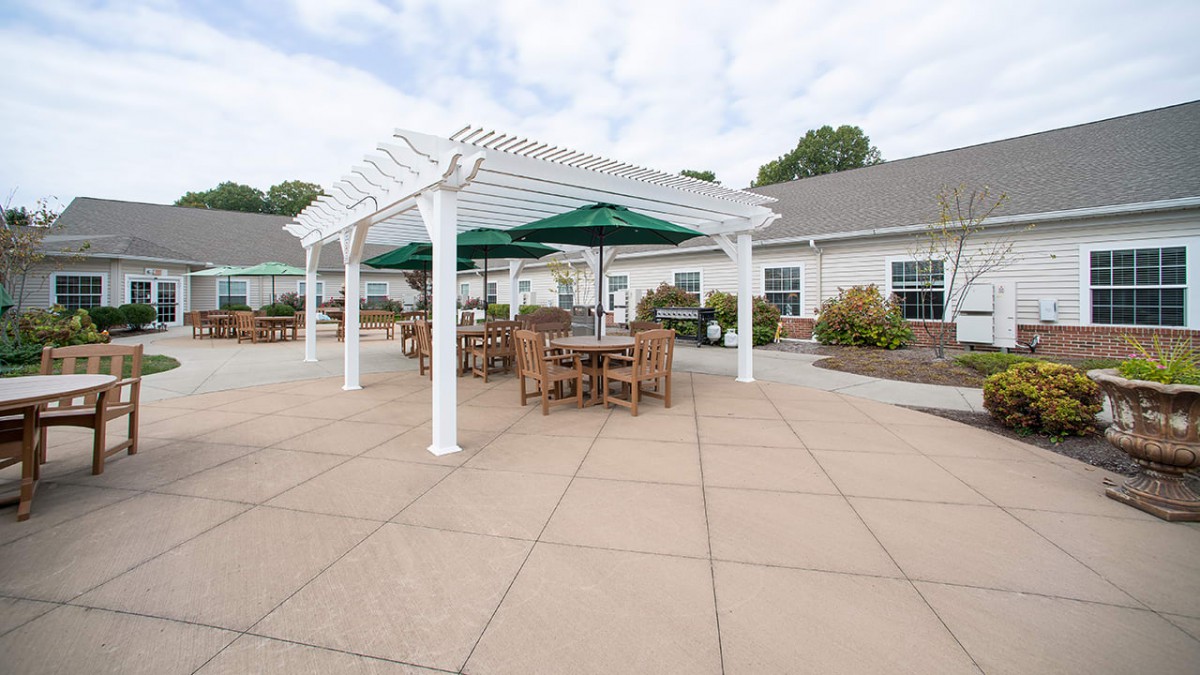 A spacious outdoor patio with tables and chairs under a pergola, featuring umbrellas for shade.