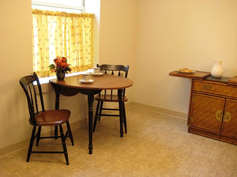A cozy kitchen corner with a small table, two chairs, and a window with yellow curtains.