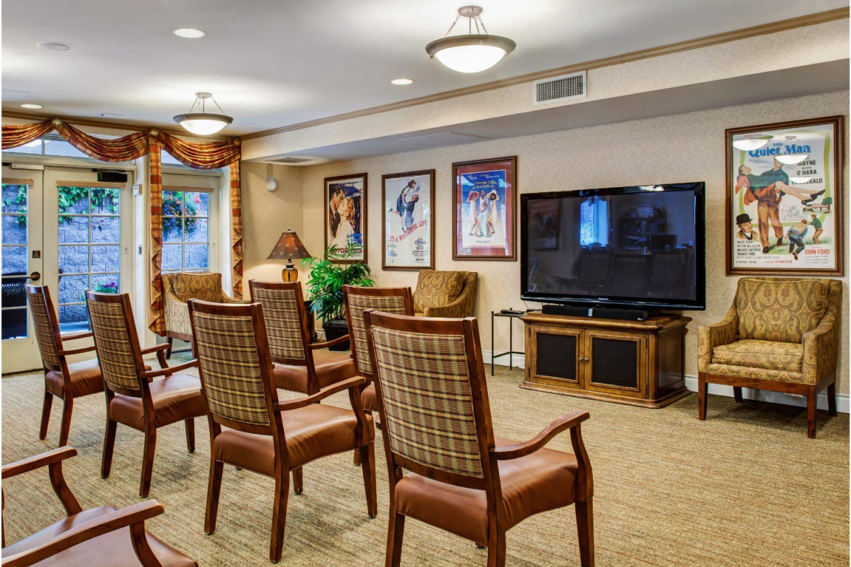 A cozy conference room with arranged chairs facing a television, adorned with framed artwork on the walls.