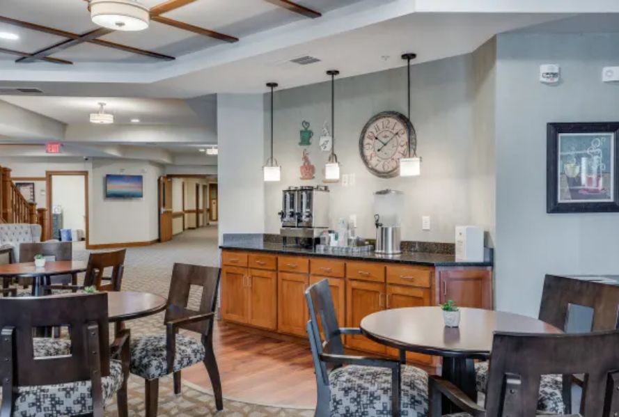 A cozy interior featuring a coffee station with tables and chairs, ambient lighting, and a large wall clock.